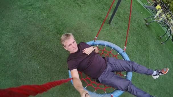 Man med selfie stick vilar på swing i parken — Stockvideo