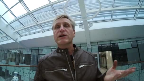 Чоловік мандрівник говорить по камері під час прогулянки в сучасній будівлі — стокове відео