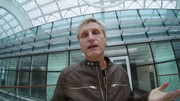 男性旅行者カメラで話している間に現代的な建物内を歩く — ストック動画
