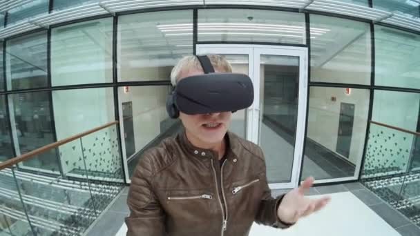 Mann mit VR-Headset spricht in modernem Gebäude vor Kamera — Stockvideo