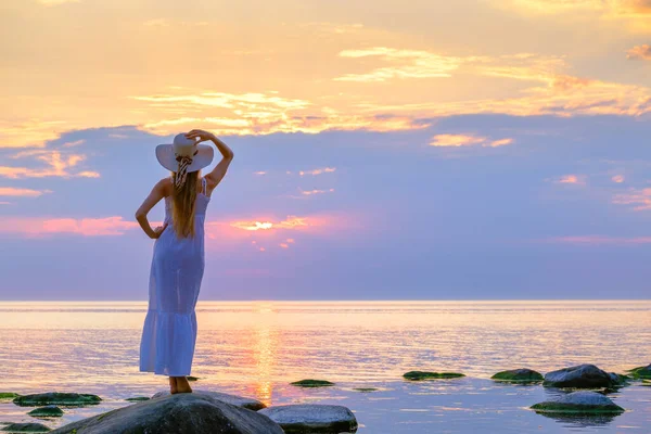 Güneş şapkalı isimsiz bir kadın denizin kenarında duruyor.