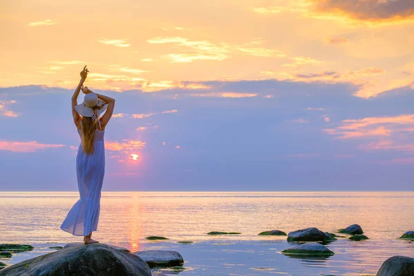 Mujer delgada en vestido disfrutando de la puesta del sol sobre el mar — Foto de Stock