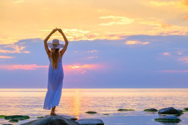 Güneş şapkalı isimsiz bir kadın denizin kenarında duruyor.