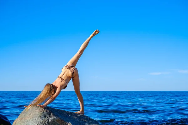 Mujer delgada haciendo yoga contra el cielo azul brillante — Foto de Stock