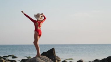 Happy woman in bodysuit dancing on rocks against ocean