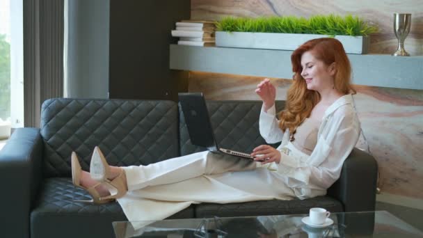 Щаслива бізнес-леді, використовуючи ноутбук на дивані — стокове відео