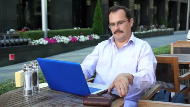Бизнесмен средних лет работает на ноутбуке и разговаривает на смартфоне — стоковое видео