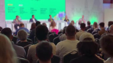 Oturmuş seyircilerle konferans sahnesi sahnenin altındaki parlak yeşil arka plan, enerjik atmosfer