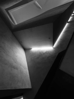 Tek renkli iç döşeme açılı duvarlar ve parlak ışık çizgisi dramatik gölgeler yaratıyor. Geometrik bileşim modern mimari, gizem ve asgari yalnızlığı çağrıştırıyor.