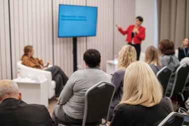 Kırmızı ceketli hoparlörlü profesyonel seminer modern konferans odasında katılımcılara fikirlerini özetliyor..