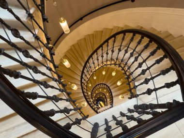 Yukarıdan aşağıya doğru kıvrılan sarmal merdiven, demir denge ve parıldayan kolye ışıklarını gösteriyor.