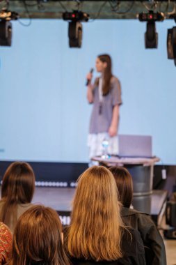 Dinamik öğrenme atmosferi yaratan ekranlar ve dizüstü bilgisayarlarla yapılan etkinlikte seyirciler sahnede sunucuyu bulanık görüyor