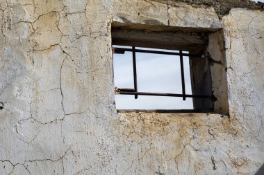 Kırsal ve yıpranmış dokuları gösteren kırık duvarda metal parmaklıklar olan küçük pencere.