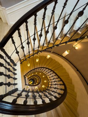 Yukarıdan görünen sarmal merdivenler işlenmiş demir parmaklıklar ahşap merdivenler ve sıcak kolye ışıkları davetkar iç atmosfer yaratıyor.