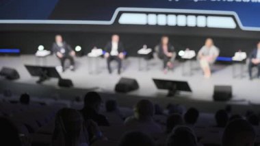 Konferans ortamında profesyonellerin oturduğu sahnede panel tartışması, seyircilerin ön planı bulanık, iş etkinliğini temsil eden konuşma, liderlik, öğrenme