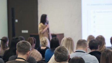 Sunucu, büyük ekran katılımcılarıyla konferans odasında kalabalığa sesleniyor. Dinleyin.