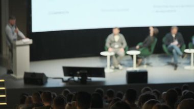 İzleyiciler dinlerken, kürsüde konuşmacı ve panelistlerle bulanık bir konferans sahnesi