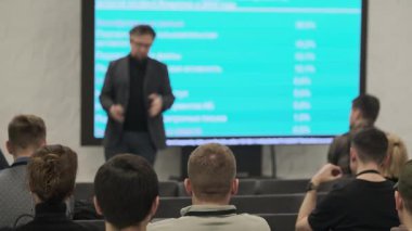 Sunucu, iş brifinginde parlak mavi ekranın yanında meşgul seyircilerin önünde duruyor.