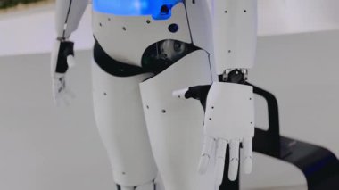 Gösterişli robot figürü temiz laboratuvar ortamında duruyor, eklemli parmakları ve mekanik eklemleri gösteriyor.