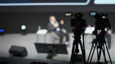 Ön planda kameralar ve görünmeyen izleyiciler ile bulanık sahne röportajı.