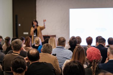 Seyirciler konferans sırasında büyük ekranlı bir odada bir konuşmacıyı dinliyorlar..