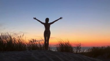 Gün batımında kumlu bir kumulda bir insanın silueti. Kollarını açıp neşe ve özgürlüğün sinyallerini veriyorlar. Sakin okyanus ufku sıcak renklerle parlar barışçıl ilham verici bir ortam yaratır..