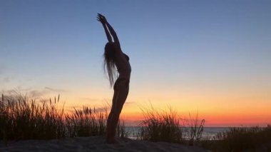 Sahilde gün batımında çimlerle uzanan bir kadın silueti. Sakinleşme zamanı..