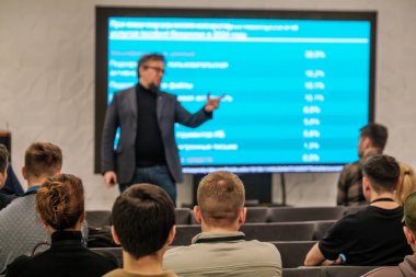 Konuşmacı özenli dinleyicilere verileri modern konferans odasına sunar. Mavi ekran istatistik ve grafikleri gösterir. Profesyonel buluşma ortamı.