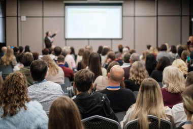 Kalabalık iş sunumunu dinliyor, modern konferans odasında odaklanmış seyirciler, profesyonel toplantı atmosferi, ağ enerjisi.