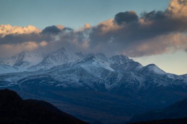 Gün batımında karlı dağlar dramatik bulutlar manzaralı ve huzurlu bir manzara yaratır..