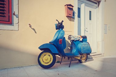 Eski mavi scooter duvarla boş sokakta park edilmiş. Vintage filtre ile işlenmiş post.
