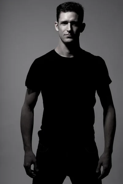 Man in black t-shirt posing on gray background.