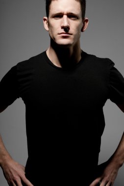Siyah t-shirt gri arka plan üzerinde poz içinde genç adam.