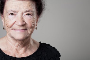 Mutlu eski Bayan gri arka plan üzerinde poz.