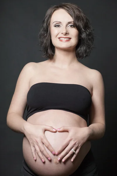 Mladá těhotná žena pózuje na černém pozadí. — Stock fotografie