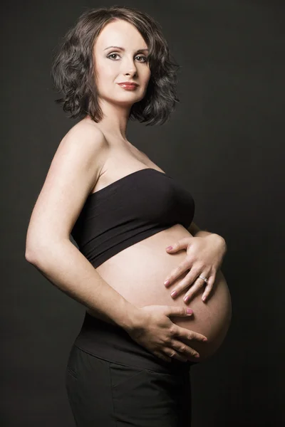 若い妊娠女性が黒い背景にポーズ. — ストック写真