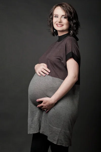 Mladá těhotná žena pózuje na černém pozadí. — Stock fotografie