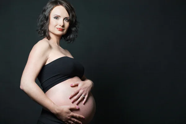 Feliz mulher grávida posando no fundo preto . — Fotografia de Stock
