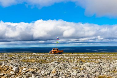 Yazın kayalık tundrada Rusya bayrağı taşıyan kırık turuncu arazi aracı.