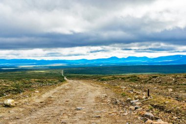 Kuzey tundrası boyunca uzanan toprak yol. Bir yaz günü Kuzey Kutbu Uralları 'ndaki dağlara.