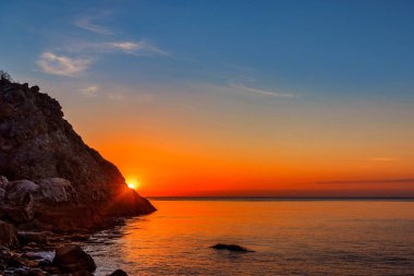 Şafak vakti kayalık bir koyda güneş sabahın erken saatlerinde denizin üzerinden doğar.