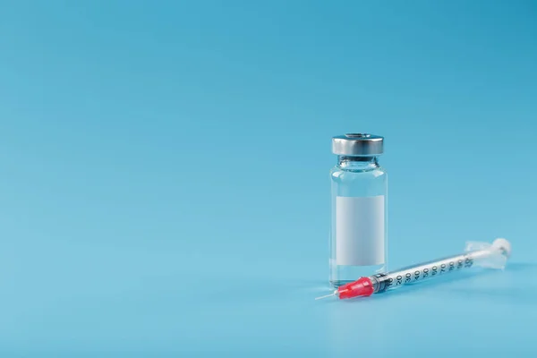 Syringe and ampoule with a vaccine against viruses and diseases on a blue background. Free space on the ampoule label for text.