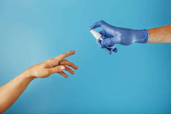 A hand in a glove with a disinfectant spray treats an unprotected hand without a glove on a blue background. The concept of prevention and prevention of the spread of viruses, infections, coronavirus diseases. Free space.