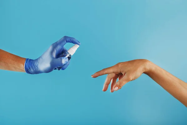 A hand in a glove with a disinfectant spray treats an unprotected hand without a glove on a blue background. The concept of prevention and prevention of the spread of viruses, infections, coronavirus diseases. Free space.