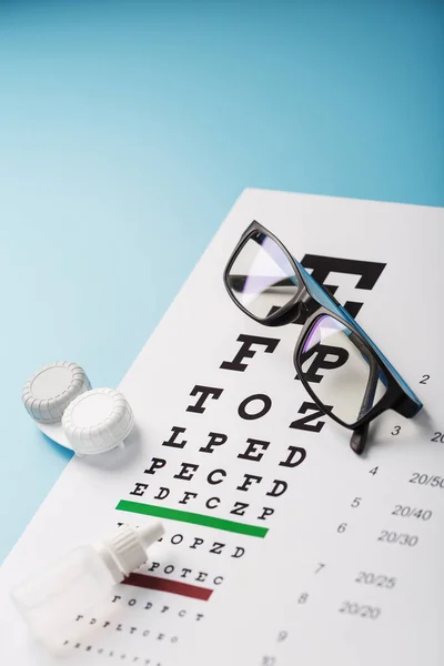 Glasses with Contact Lenses, drops and an Optometrist\'s Eye Test Chart On a Blue Background. The View From The Top. Free space