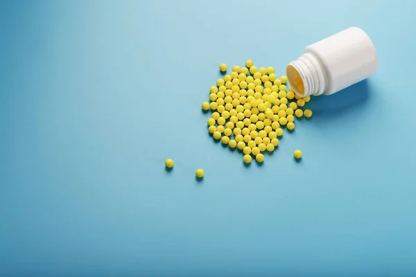 Yellow vitamin C capsules spilled out of a white jar against a blue background. Take care of your health. Vitamins and minerals. Free space