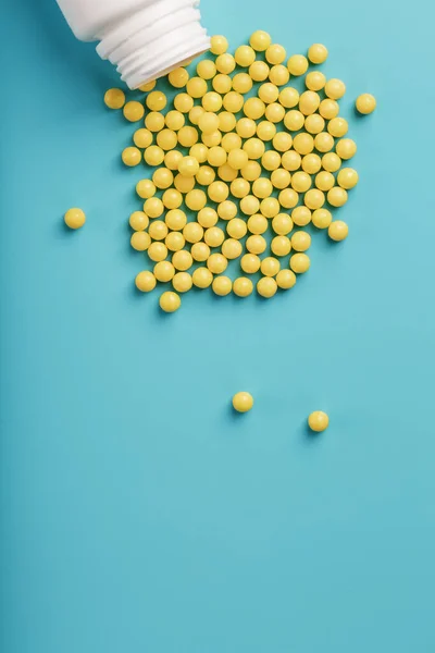 Yellow vitamin C capsules spilled out of a white jar against a blue background. Take care of your health. Vitamins and minerals. Free space