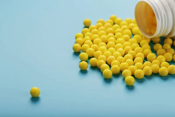 Yellow vitamin C capsules spilled out of a white jar against a blue background.