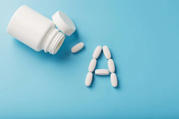 Vitamin A pills fell out of a white jar on a blue background.