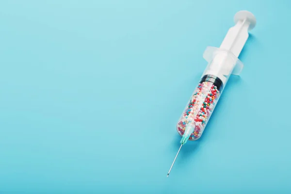 Syringe filled with colorful nano balls on a light blue background. Innovative medical concept of a cure for viruses and diseases. Gene modification